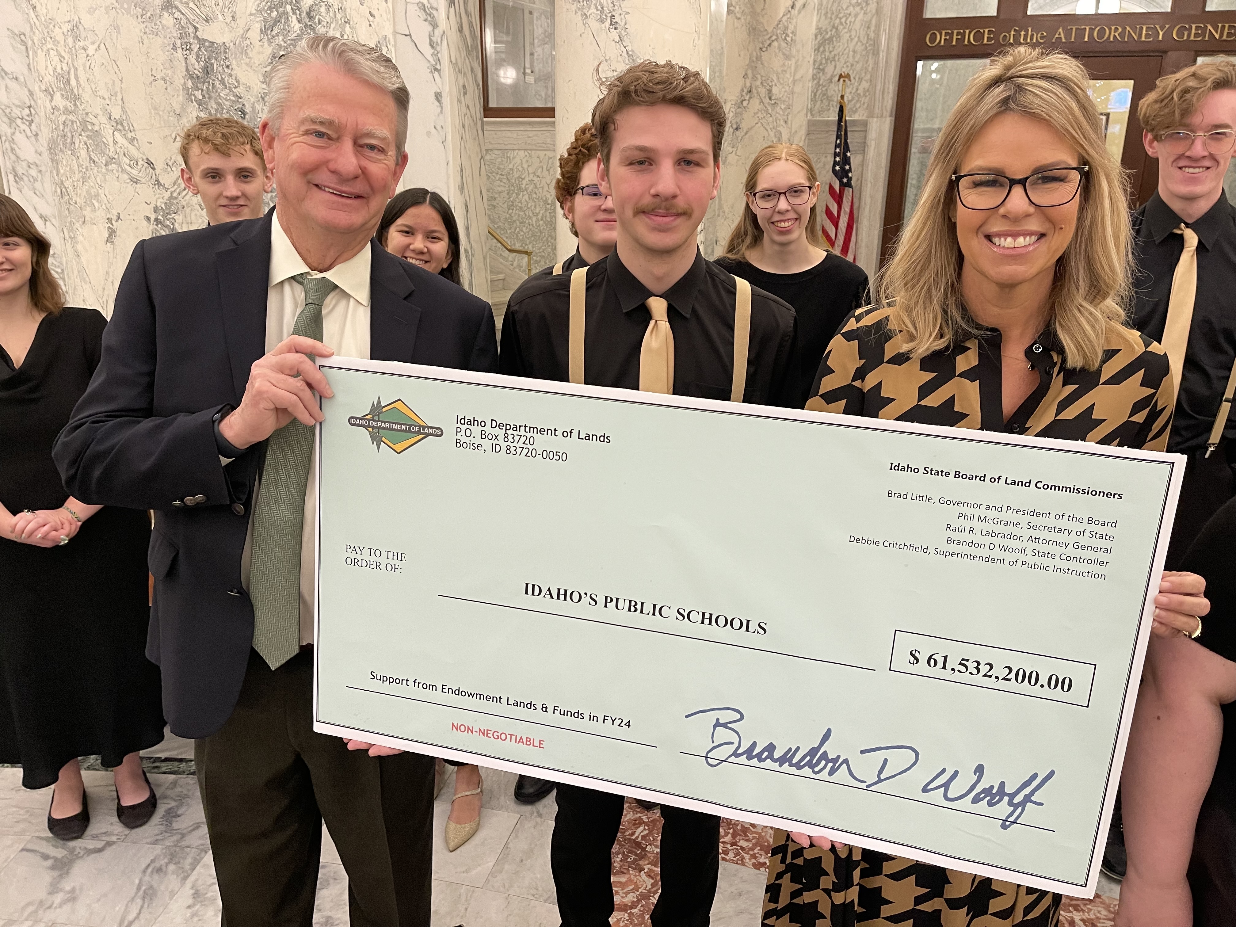A ceremonial check held by Idaho's Governor and Secretary of Public Instruction with a choir student between them.